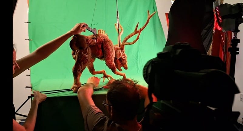 Puppeteers operating a horned creature puppet in front of a green screen