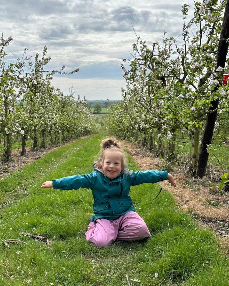 Sophia smiling with her arms outstretched in an orchard