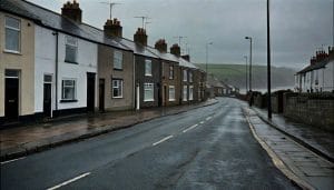 A quiet English coastal town street with terraced houses and a grey sea visible in the distance, illustrating themes of coastal deprivation