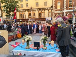Mourners around a candlelit memorial table draped with a Maidstone Gurkha Nepalese Community banner in Jubilee Square, Maidstone.