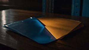 Two blank document folders overlapping on a dark desk, one lit blue and one lit amber, representing two contradictory official answers